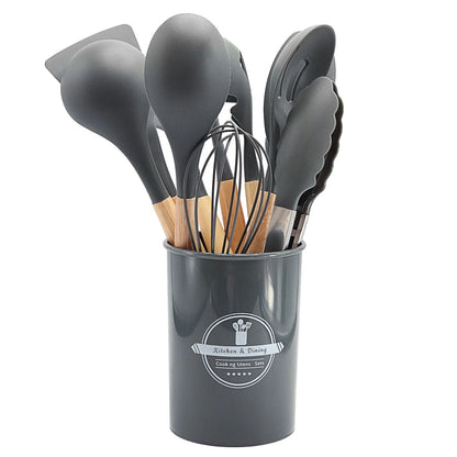 Set of gray kitchen utensils including spoons and a whisk in a cylindrical holder on a white background.