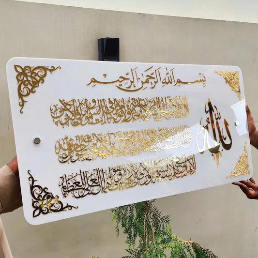 Decorative sign with Arabic calligraphy and gold accents held by a person.